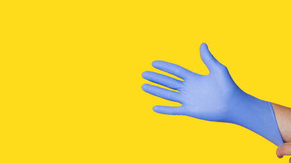 Hands wearing a blue latex glove, isolated on yellow background