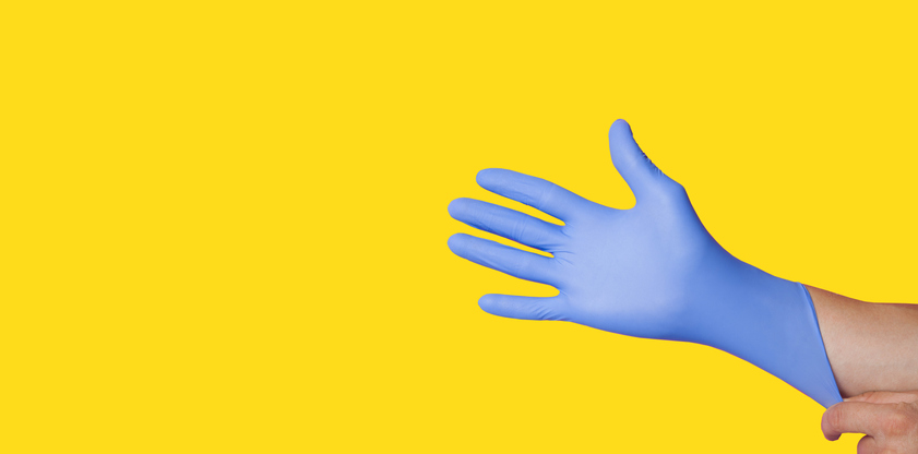 Hands wearing a blue latex glove, isolated on yellow background