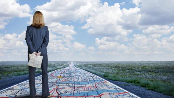 Businesswoman Stands On Long Road With Road Map Painted On It
