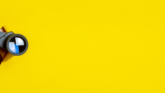 Female,Hand,Holds,Black,Binoculars,On,A,Yellow,Background.,Journey,